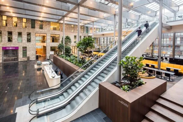 Moderne en lichte ontvangsthal aan de Prinses Beatrixlaan met roltrappen, groenvoorziening en een receptiebalie.